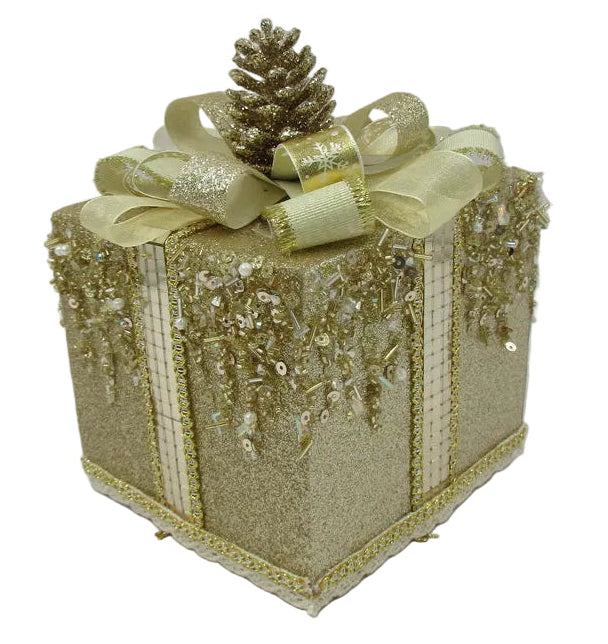 A glittery gold gift box ornament decorated with a gold ribbon bow, a small gold pinecone, and hanging gold sequins.