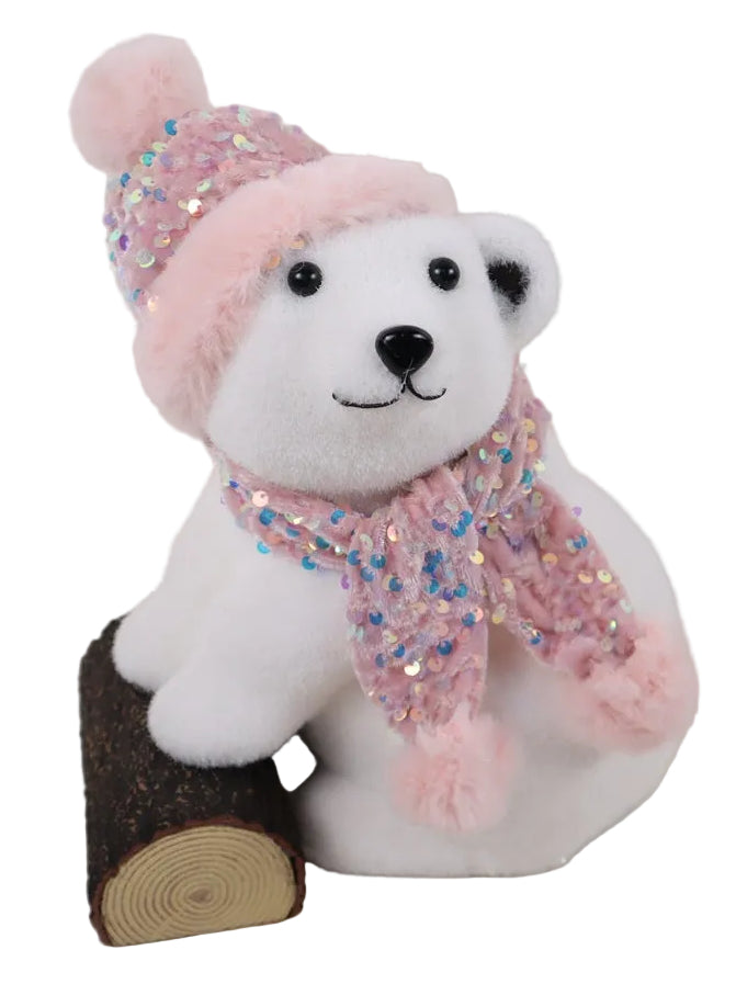 A white bear wearing a pink hat and scarf, sitting next to a brown log.