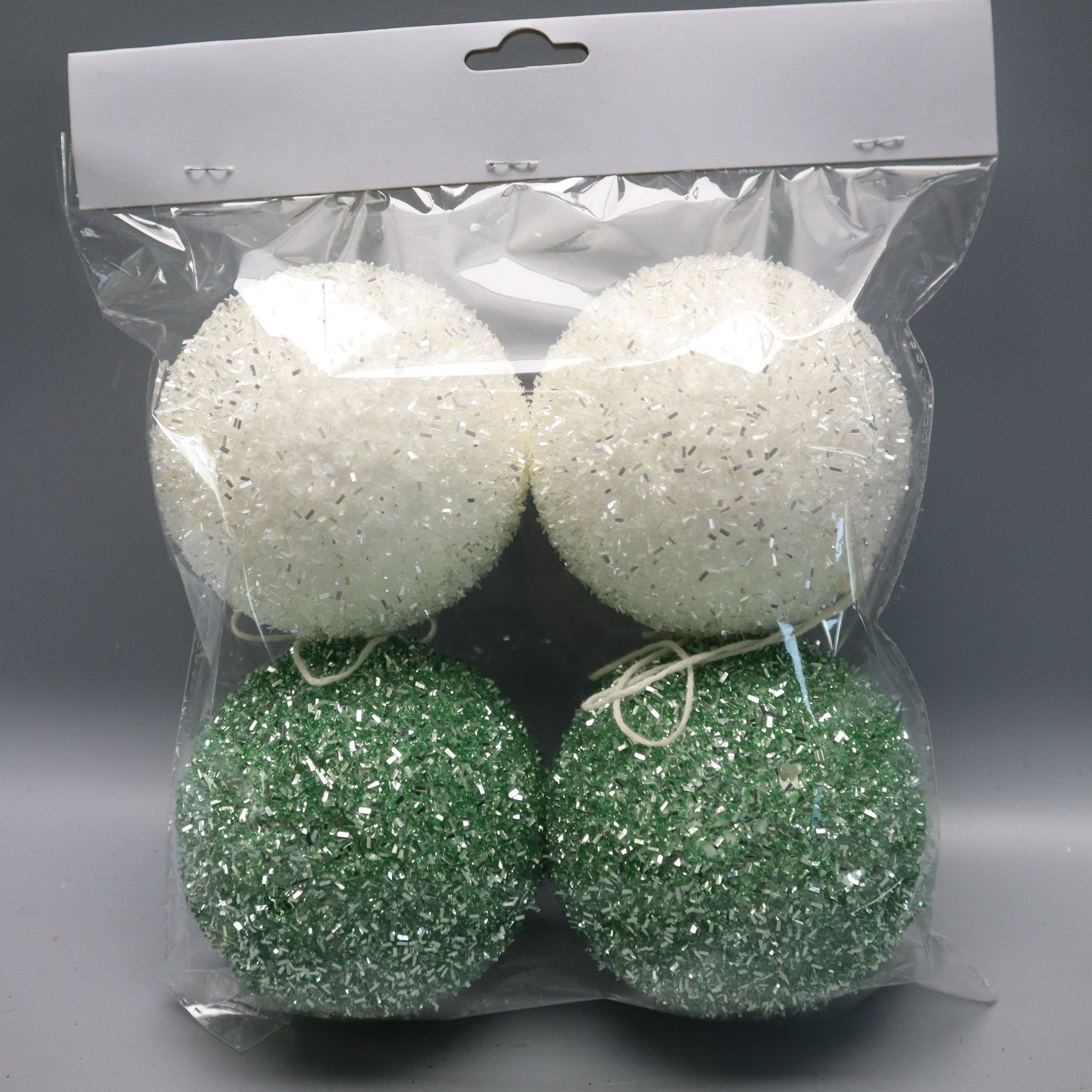 Four glittery Christmas ornaments in two colors: two white and two green, packaged in a clear plastic bag with a white cardboard hanger.