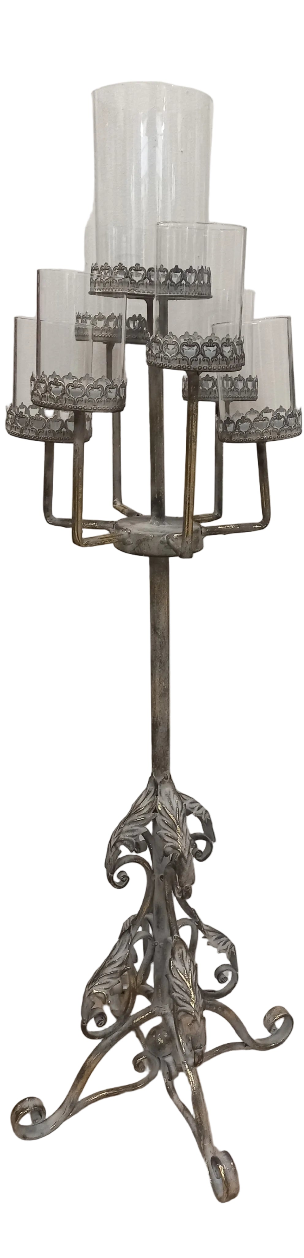 A silver metal candle stand with a decorative base, holding seven cylindrical candle holders.