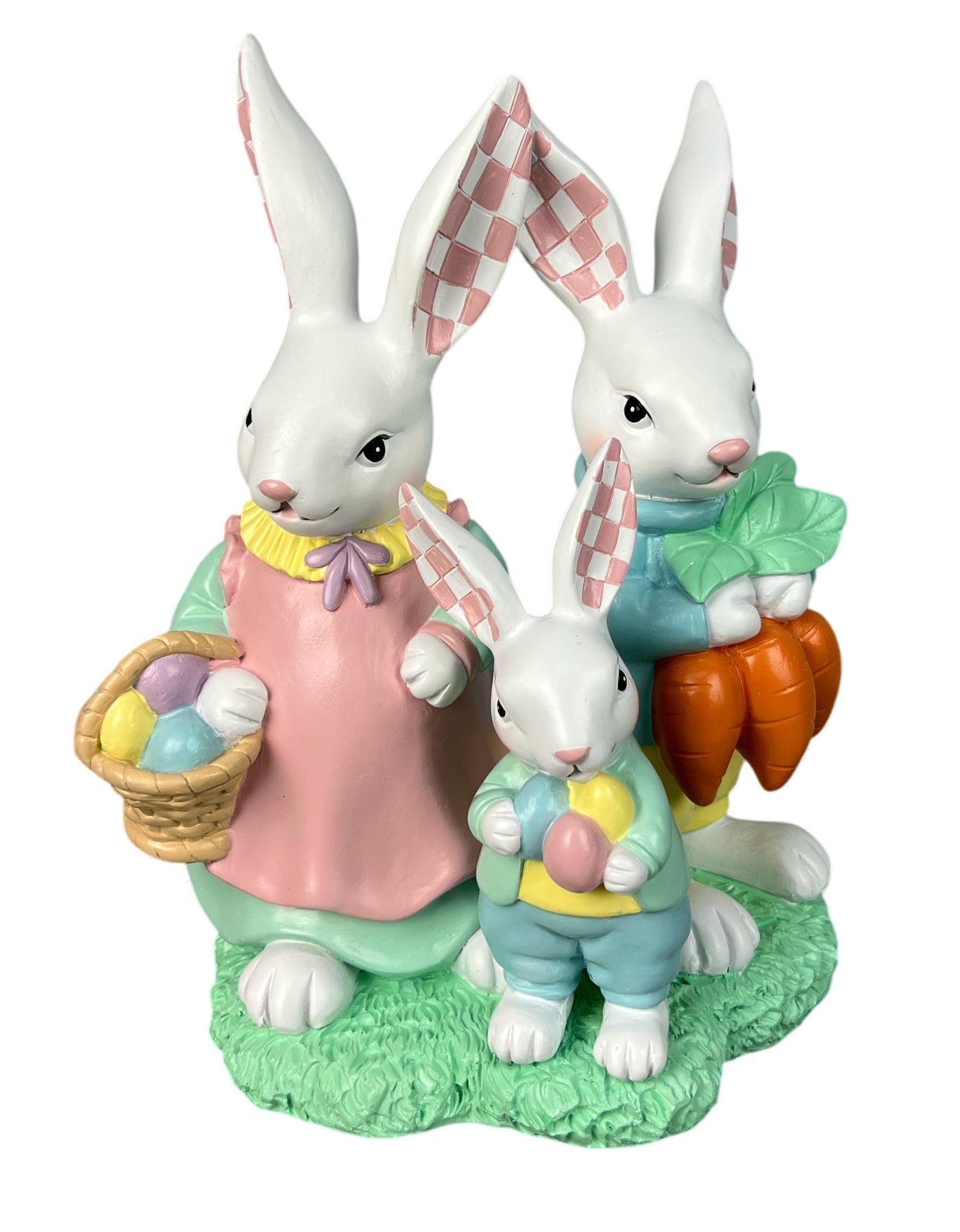 A white Easter bunny figurine with three bunnies dressed in pastel clothing, holding a basket of eggs, carrots, and Easter eggs, set on a green textured base.