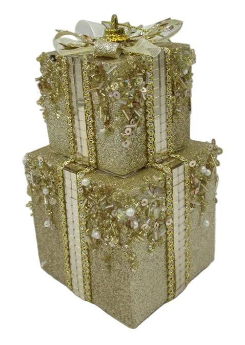 A decorative two-tiered gift box ornament in glittery champagne gold, embellished with sequins, beads, and a matching gold ribbon and bow on top.